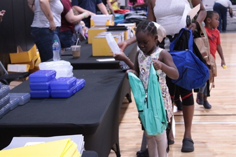 young girl adding school supplies to backpack