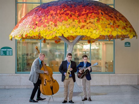 people with instruments standing in front of rainbow tree sculpture