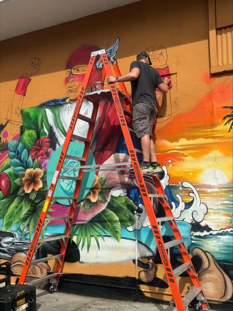 Artist on tall ladder painting a wall mural.
