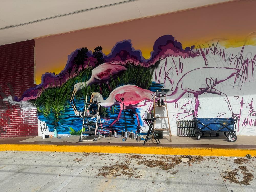 Artist painting outside mural of pink flamingos.
