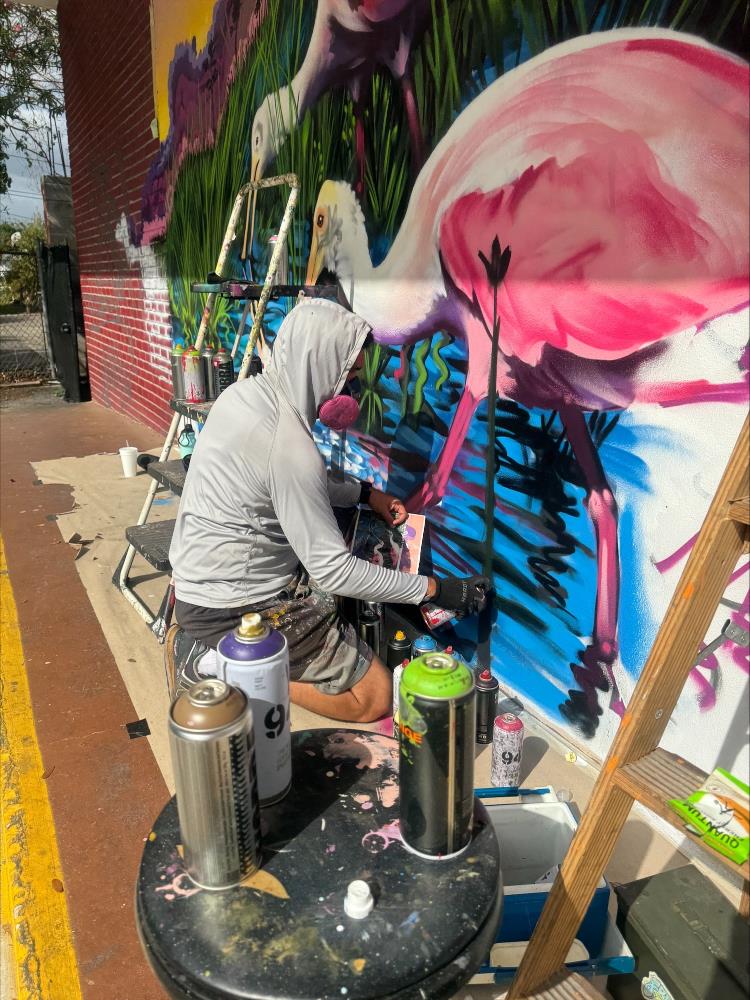 Artist painting pink flamingo on outside mural.