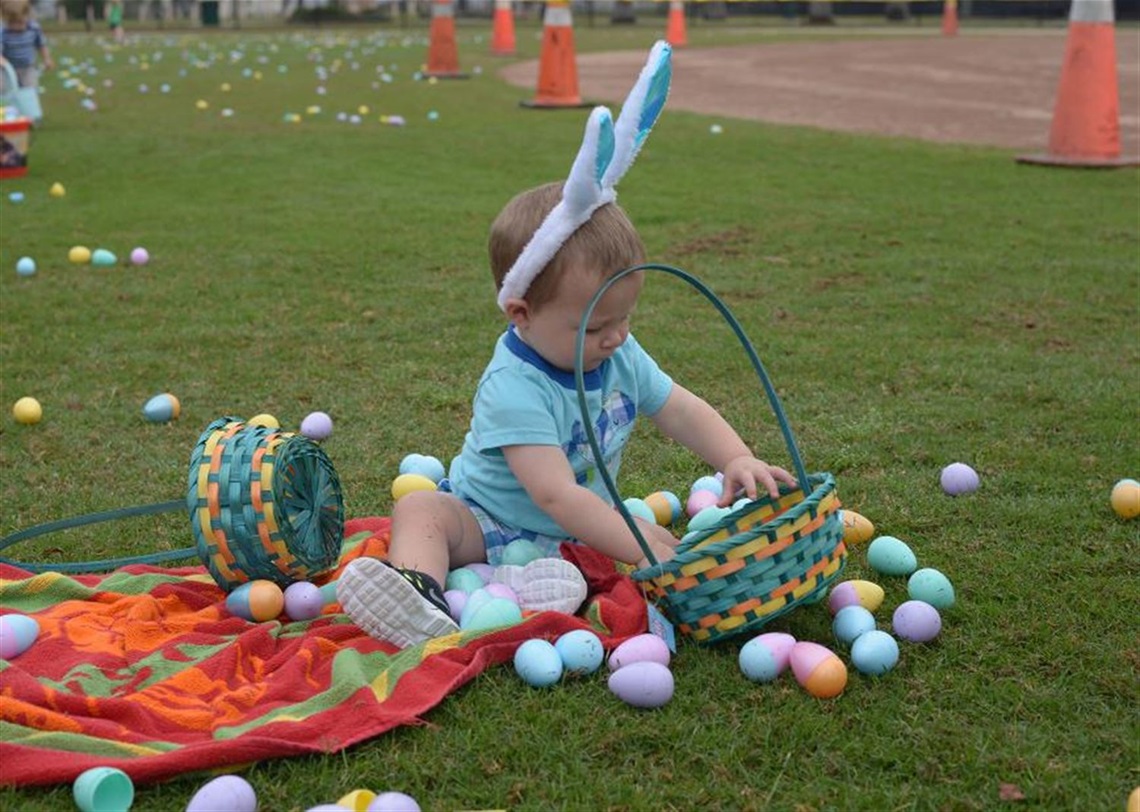 toddler sitting on grass with two easter egg baskets wearing rabbit ears