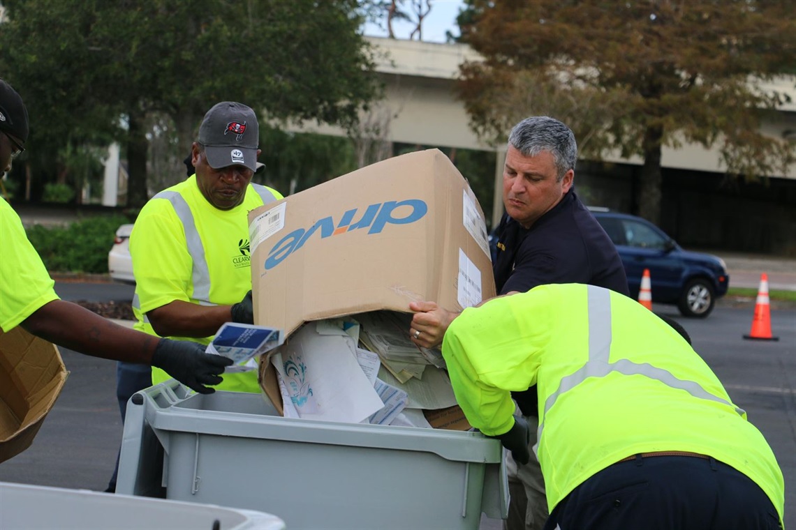 Workers in high visibility shirts dumping trash into a bin.